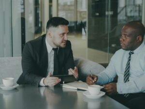 Zwei Männer im Geschäftsgespräch mit Kaffee am Tisch, diskutieren gemeinsam Arbeitsdokumente in modernem Büro