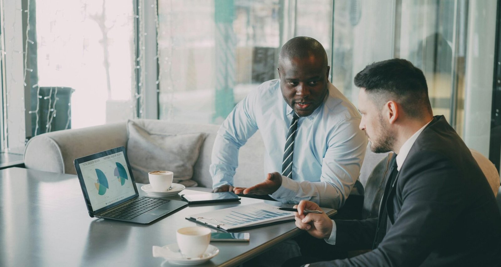 Zwei Geschäftsleute betrachten und diskutieren gemeinsam verschiedene Diagramme auf einem Laptop am Schreibtisch.