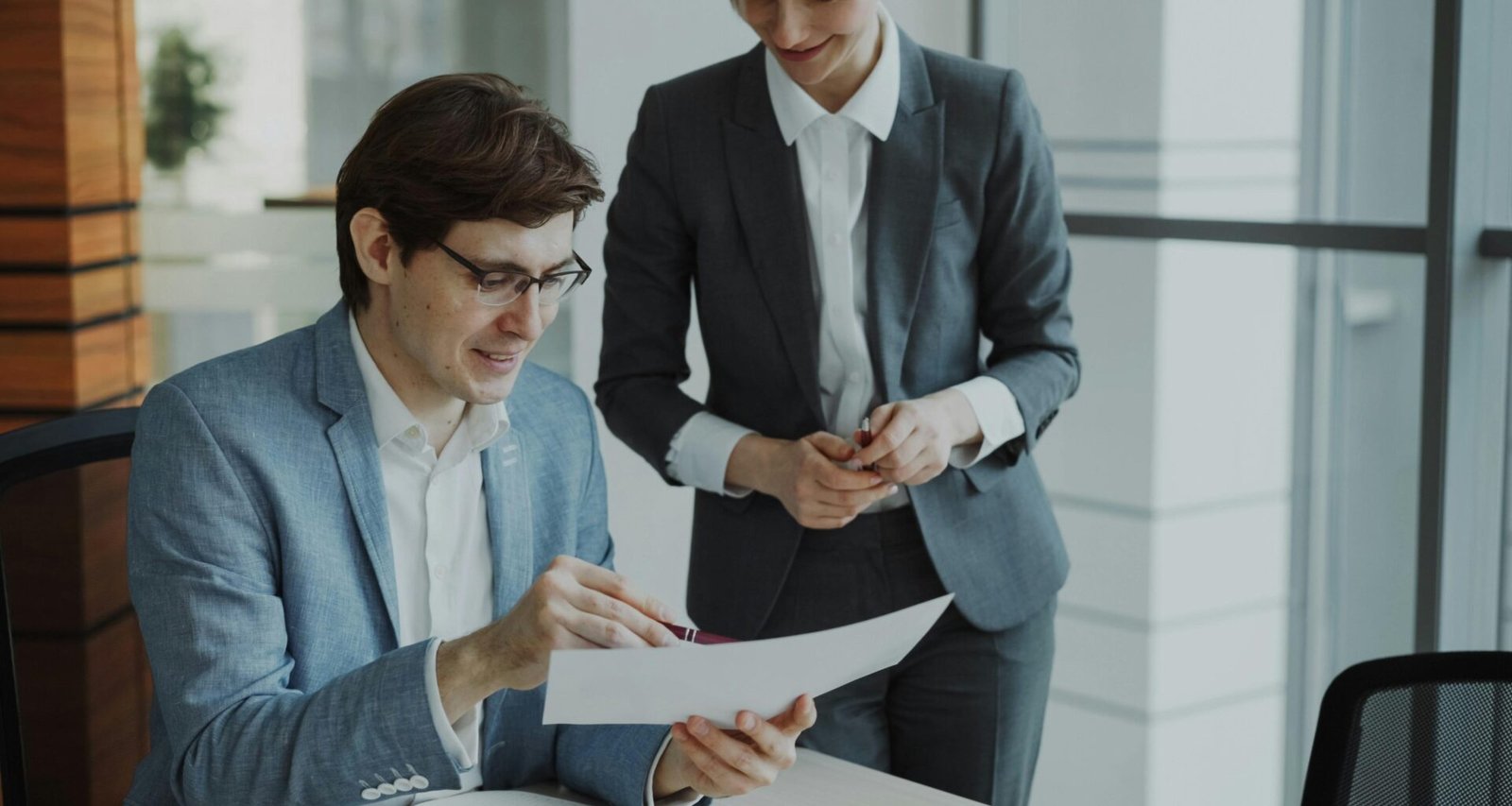Zwei Geschäftspersonen sitzen an einem Tisch und besprechen gemeinsam Unterlagen und Geschäftsanalysen.