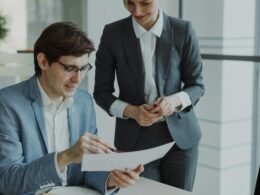 Zwei Geschäftspersonen sitzen an einem Tisch und besprechen gemeinsam Unterlagen und Geschäftsanalysen.