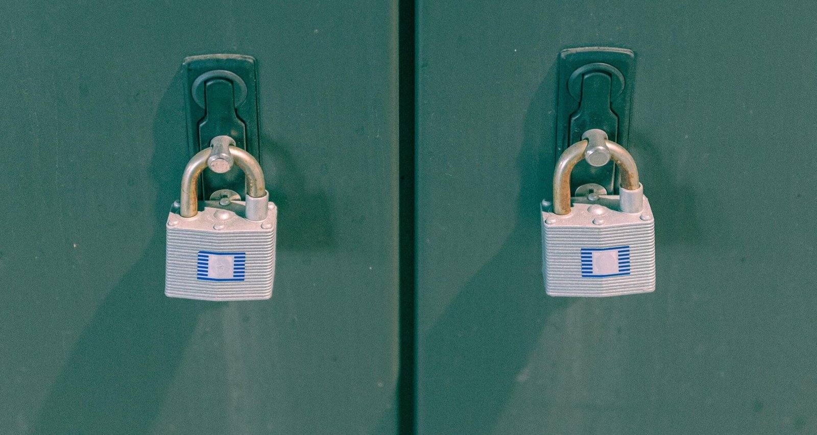 Zwei nebeneinander stehende grüne Spinde, beide mit silbernen Vorhängeschlössern gesichert, vor neutralem Hintergrund