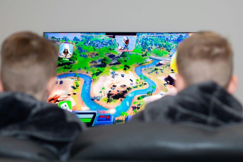 Zwei Jungen sitzen vor einem Fernseher und spielen ein Videospiel mit Controllern in einem modern eingerichteten Wohnzimmer.