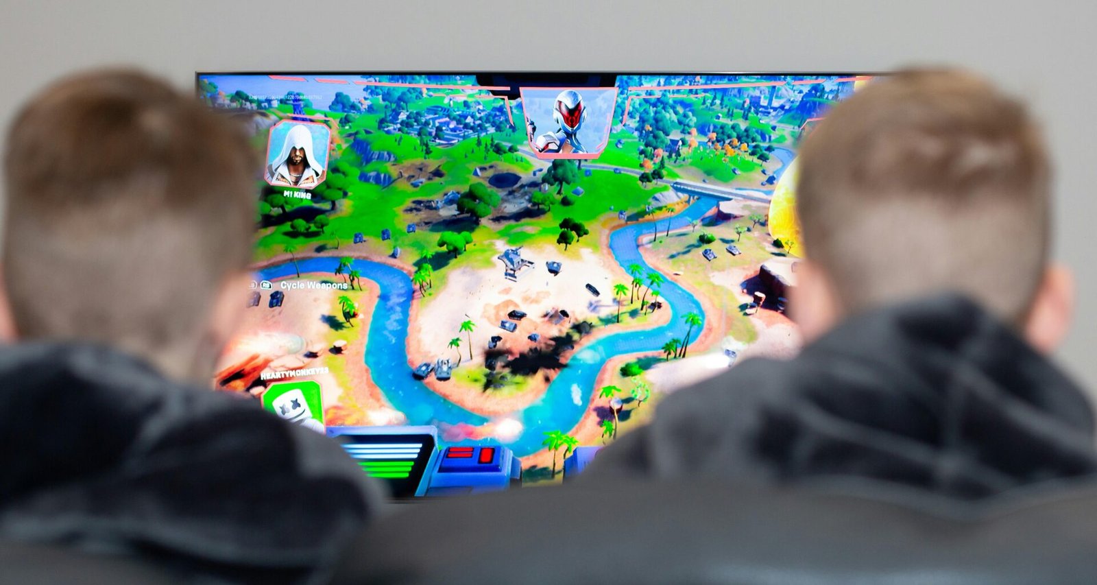 Zwei Jungen sitzen vor einem Fernseher und spielen ein Videospiel mit Controllern in einem modern eingerichteten Wohnzimmer.