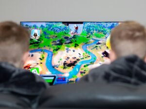 Zwei Jungen sitzen vor einem Fernseher und spielen ein Videospiel mit Controllern in einem modern eingerichteten Wohnzimmer.