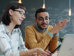Zwei Kollegen arbeiten gemeinsam an einem Laptop im Büro und tauschen Ideen für ein Projekt aus