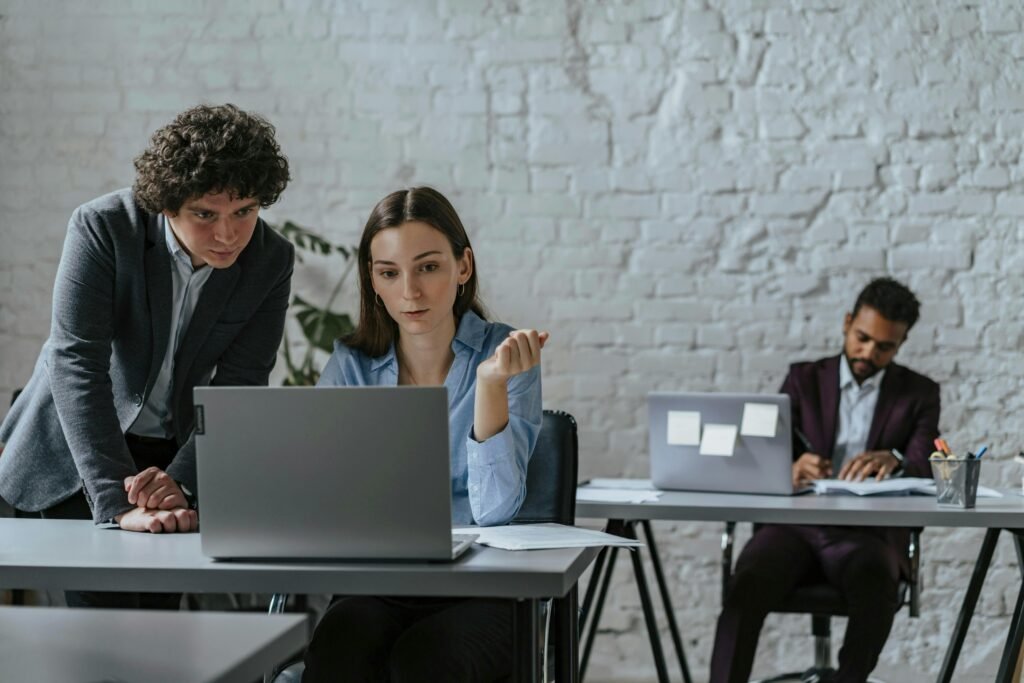 Zwei Kollegen sitzen im Büro und nutzen gemeinsam einen Laptop zur Zusammenarbeit an einem Projekt.