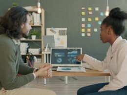 Zwei Kollegen sitzen zusammen und analysieren gemeinsam Geschäftsdaten auf einem Laptop am Arbeitsplatz.