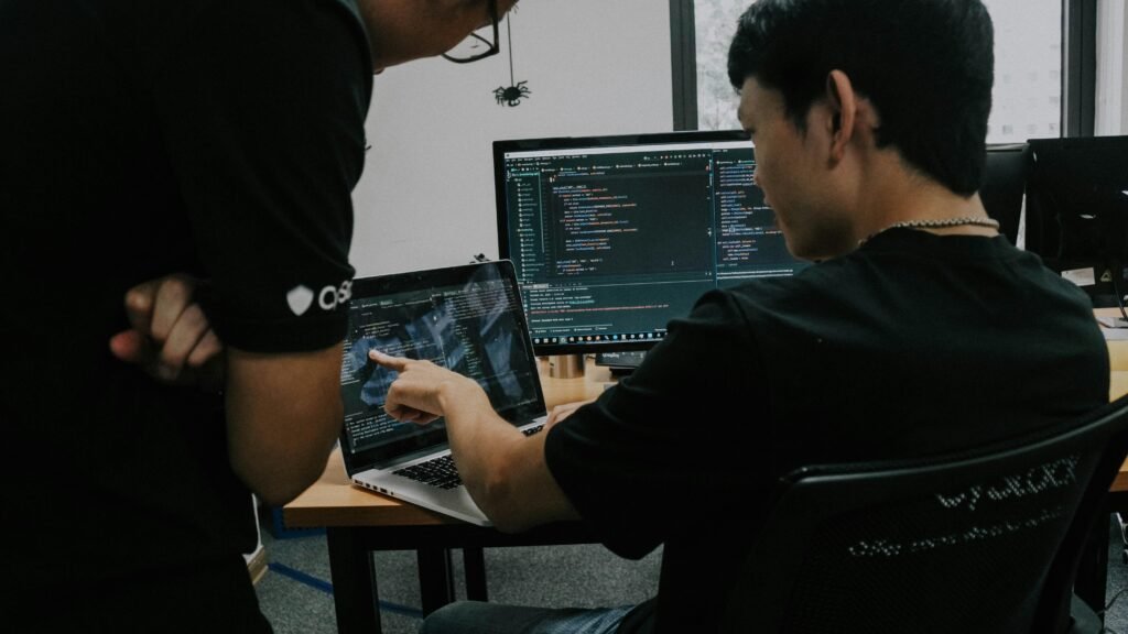 Zwei Männer arbeiten an Schreibtischen mit Computern in einem offenen, modernen Büro mit großem Fenster.