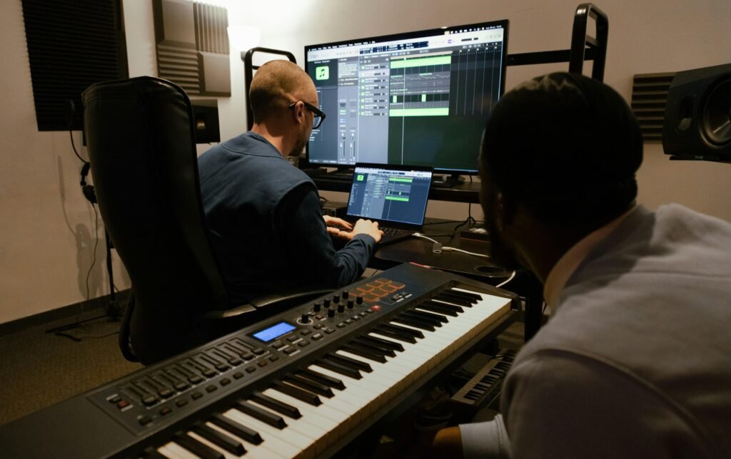 Zwei Männer sitzen gemeinsam an Computern und Musiktechnik in einem professionellen Tonstudio.
