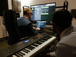 Zwei Männer sitzen gemeinsam an Computern und Musiktechnik in einem professionellen Tonstudio.