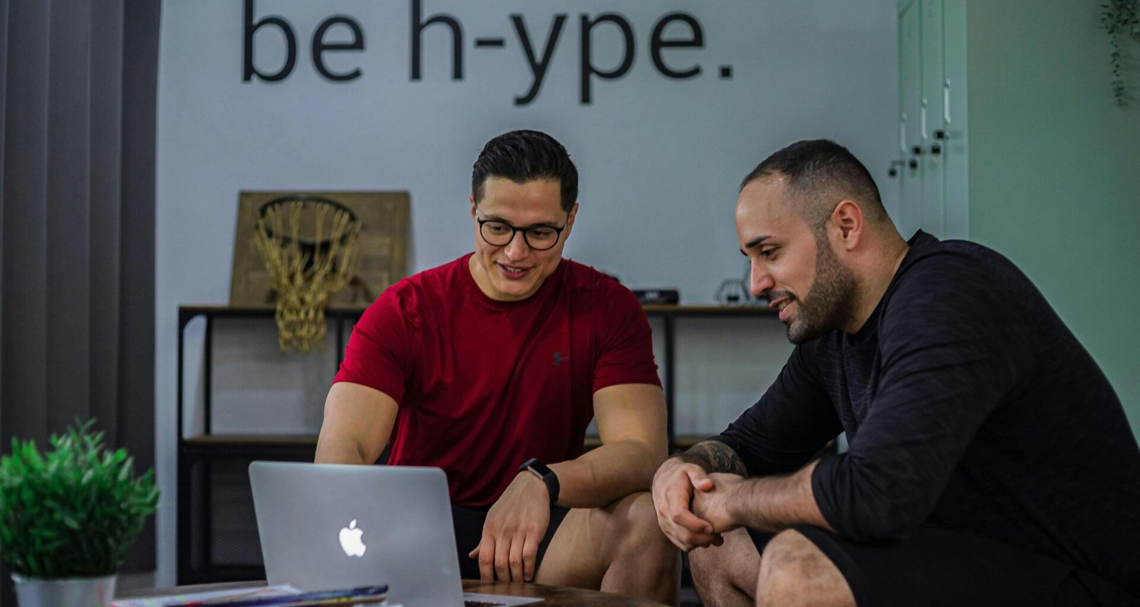 Zwei Männer sitzen nebeneinander an einem Kaffeetisch und betrachten gemeinsam einen Laptop