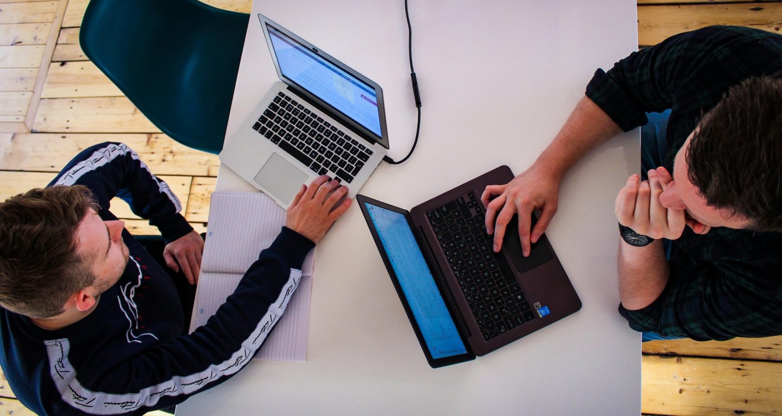 Zwei Männer sitzen an einem Tisch und arbeiten konzentriert an ihren Laptops in einem modernen Büro.