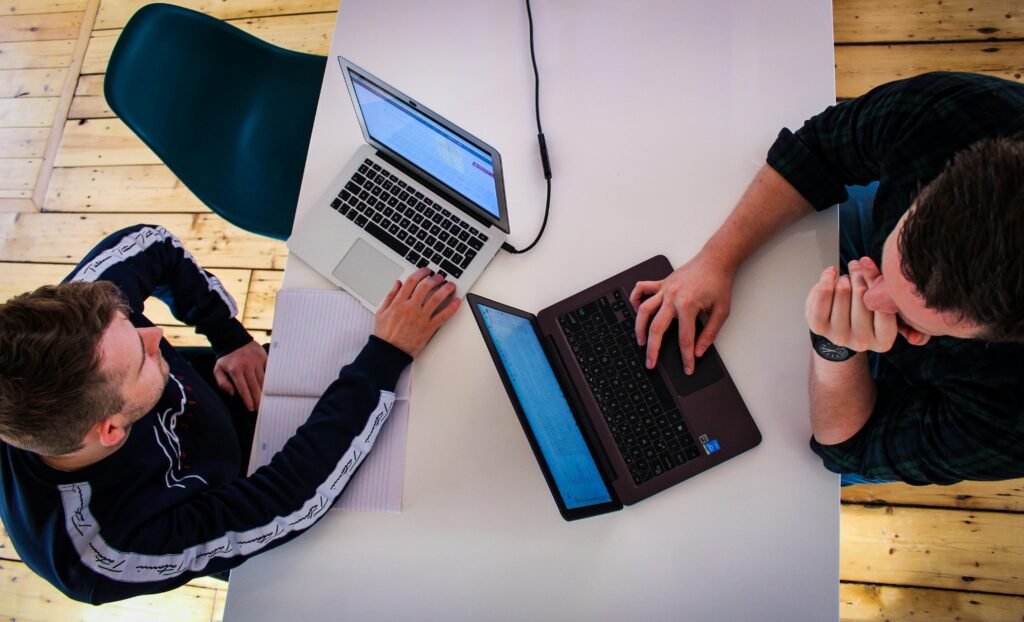 Zwei Männer arbeiten gemeinsam an einem Tisch mit Laptops in einem modernen Büro, Ansicht von der Seite