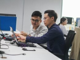 Zwei Männer sitzen an einem Schreibtisch und betrachten zusammen einen Laptop während der Arbeit