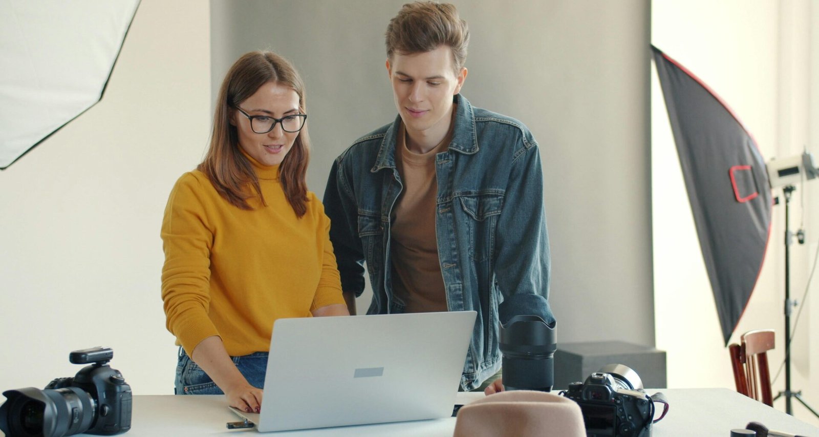 Zwei Menschen sitzen nebeneinander in einem Studio und schauen gemeinsam auf den Bildschirm eines Laptops.