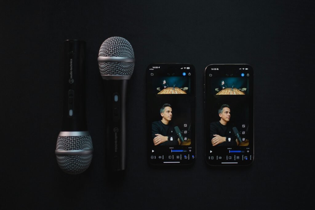 Zwei Mikrofone stehen neben zwei Smartphones, die beide einen Podcast anzeigen. Technik-Setup für Podcast-Aufnahmen.