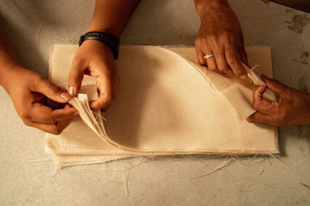Zwei Personen sitzen bei der gemeinsamen Arbeit an einem Stoffstück an einem Tisch mit Arbeitsmaterialien