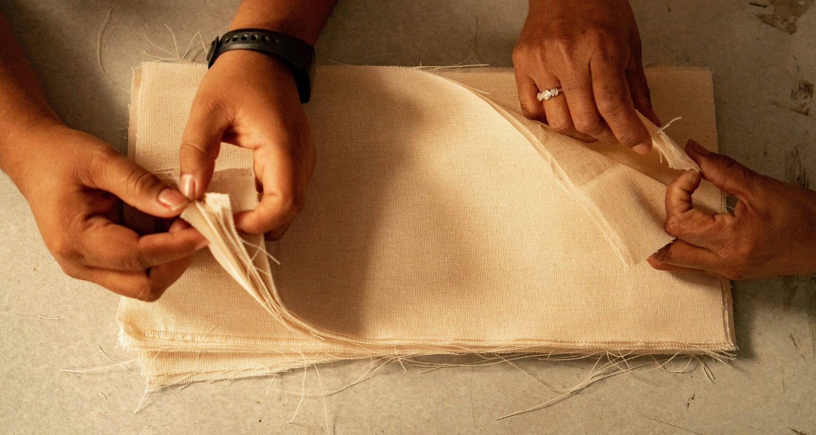 Zwei Personen sitzen bei der gemeinsamen Arbeit an einem Stoffstück an einem Tisch mit Arbeitsmaterialien