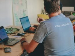 Zwei Personen sitzen an einem Tisch und arbeiten jeweils an ihren Laptops in einem modernen Arbeitsumfeld.