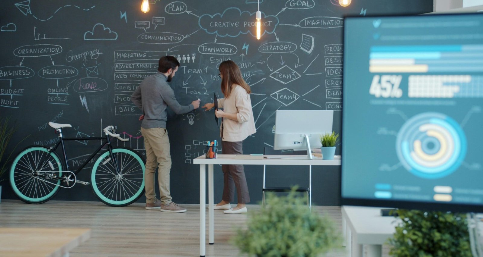 Zwei Menschen arbeiten zusammen an einem Whiteboard, ein Fahrrad steht daneben, Fokus auf Zusammenarbeit und Kreativität.