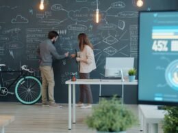 Zwei Menschen arbeiten zusammen an einem Whiteboard, ein Fahrrad steht daneben, Fokus auf Zusammenarbeit und Kreativität.