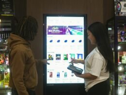 Zwei Personen stehen vor einem digitalen Display und interagieren miteinander in einer modernen Umgebung.