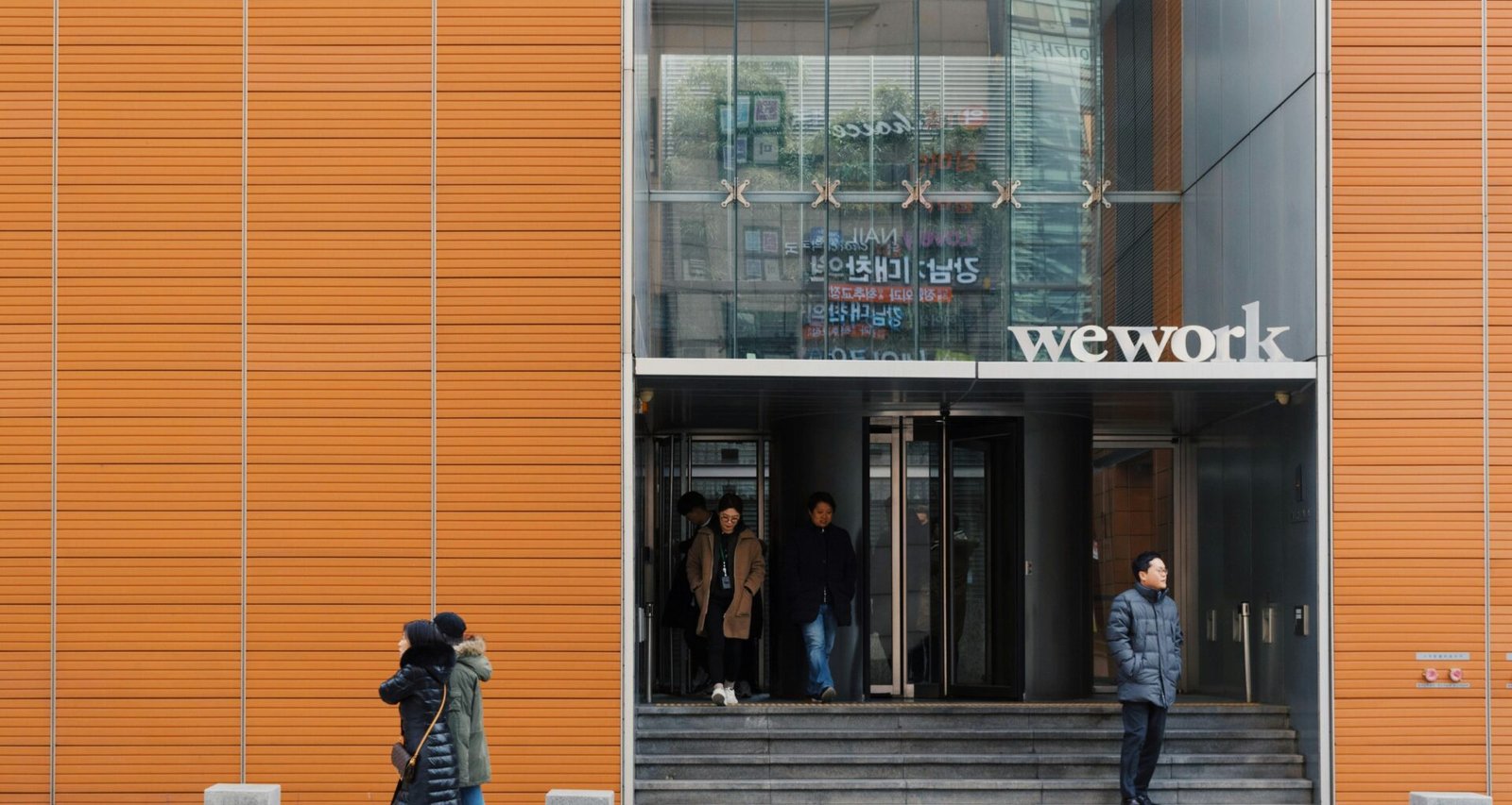 Zwei Personen spazieren auf dem Gehweg vor einem modernen Wework-Gebäude in einer Stadtumgebung