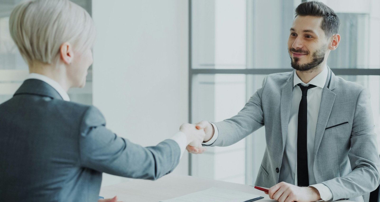 Zwei Geschäftspersonen sitzen sich an einem Tisch gegenüber und geben sich zur Besiegelung eines Deals die Hand.