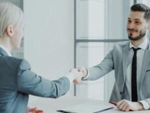 Zwei Geschäftspersonen sitzen sich an einem Tisch gegenüber und geben sich zur Besiegelung eines Deals die Hand.