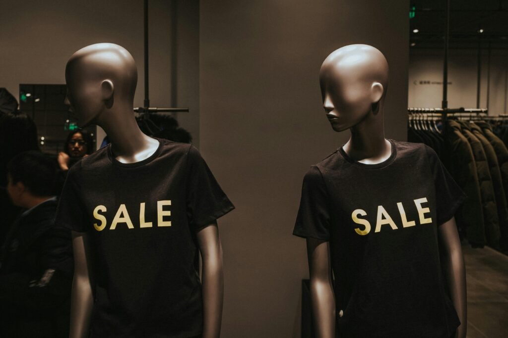 Zwei Schaufensterpuppen mit schwarzen Sale-Grafik-T-Shirts, präsentiert als Werbemotiv in einem Geschäft.