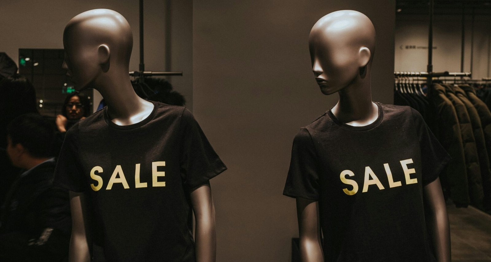 Zwei Schaufensterpuppen mit schwarzen Sale-Grafik-T-Shirts, präsentiert als Werbemotiv in einem Geschäft.