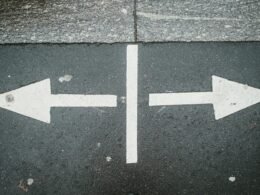 Zwei weiße Pfeile, die sich auf einer Asphaltfläche in entgegengesetzte Richtungen zeigen, als Symbol für unterschiedliche Wege.