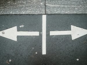 Zwei weiße Pfeile, die sich auf einer Asphaltfläche in entgegengesetzte Richtungen zeigen, als Symbol für unterschiedliche Wege.