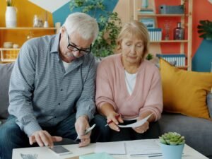 Ein älteres Paar sitzt am Tisch in ihrem Wohnzimmer und sieht sich gemeinsam verschiedene Dokumente an