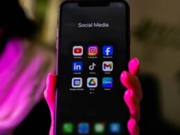 Ein Smartphone, auf dessen Bildschirm verschiedene Social Media App-Symbole abgebildet sind, liegt auf einer Oberfläche.