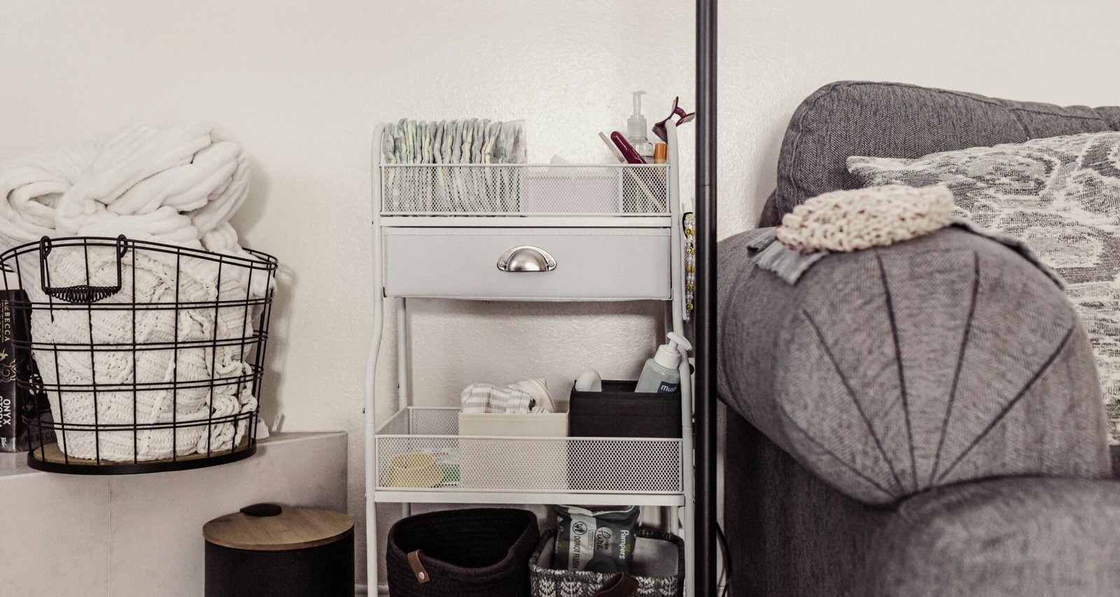 Ein Aufbewahrungswagen mit mehreren Körben steht direkt neben einem Sofa im Wohnraum, ideal zum Verstauen von Alltagsgegenständen.