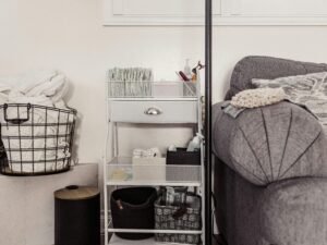 Ein Aufbewahrungswagen mit mehreren Körben steht direkt neben einem Sofa im Wohnraum, ideal zum Verstauen von Alltagsgegenständen.