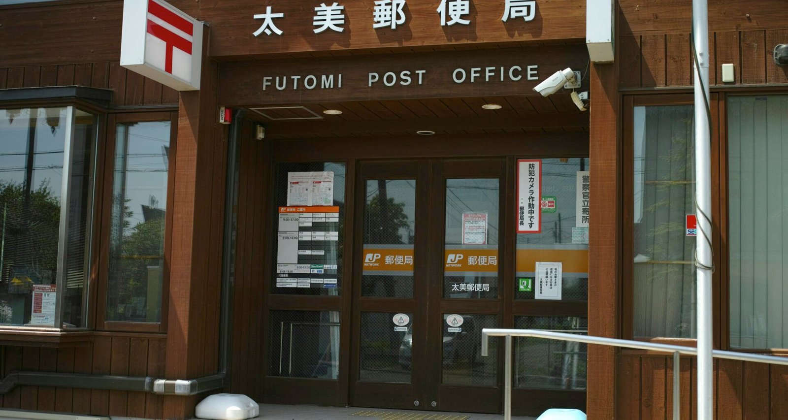 Detaillierte Aufnahme eines Futomi Postamt-Schildes mit japanischen Schriftzeichen und Symbol vor einfarbigem Hintergrund