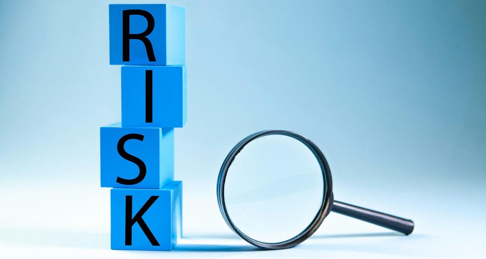 Blaue Bausteine mit dem Wort Risk liegen neben einer Lupe auf einem weißen Hintergrund – Symbol für Risikoanalyse im Online-Marketing.