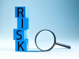Blaue Blöcke mit dem Wort Risk liegen neben einer Lupe, Symbol für Risikoanalyse im technischen und digitalen Umfeld.