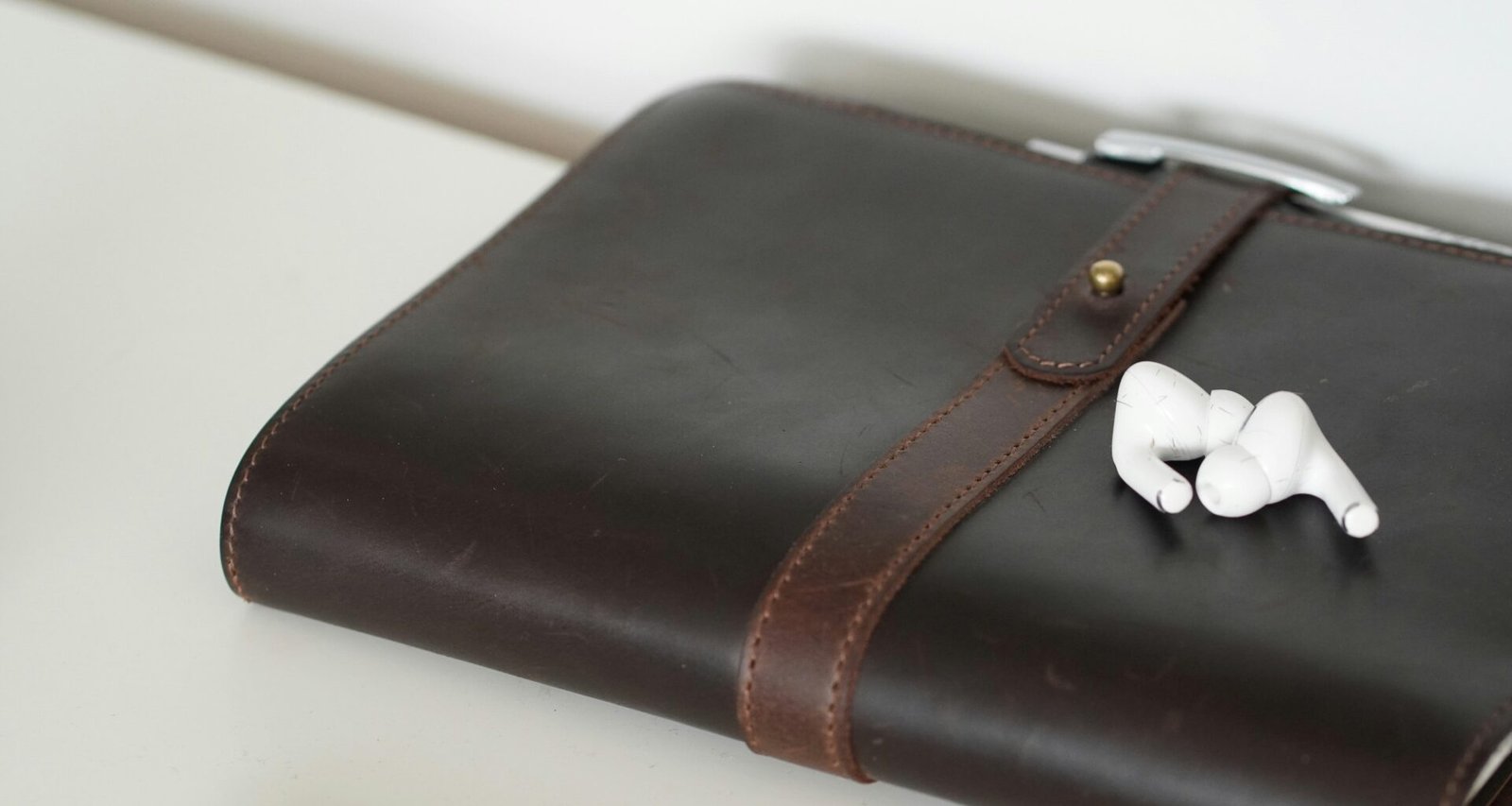 Braunes Notizbuch aus Leder mit weißen Earbuds darauf, ideal für Notizen und Musik, fotografiert auf einem Tisch