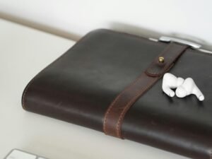 Braunes Notizbuch aus Leder mit weißen Earbuds darauf, ideal für Notizen und Musik, fotografiert auf einem Tisch
