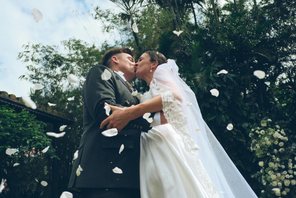 Braut und Bräutigam küssen sich im Freien, während Blütenblätter bei ihrer Hochzeit auf sie niederfallen