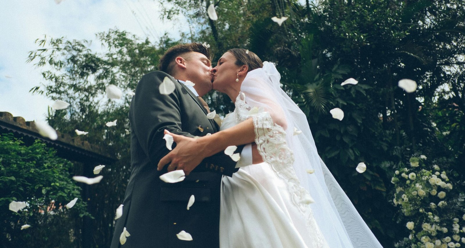 Braut und Bräutigam küssen sich im Freien, während Blütenblätter bei ihrer Hochzeit auf sie niederfallen