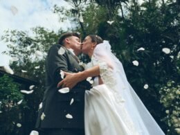 Braut und Bräutigam küssen sich im Freien, während Blütenblätter bei ihrer Hochzeit auf sie niederfallen