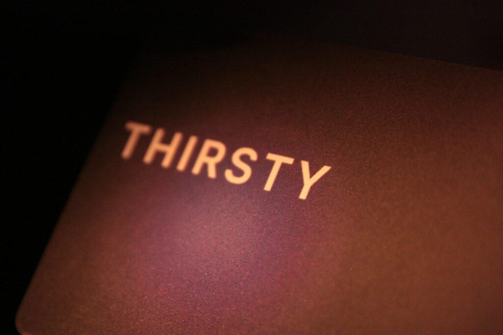 Das Wort "thirsty" steht weiß geschrieben auf einer dunkel gehaltenen Oberfläche, minimalistisch und klar fotografiert.