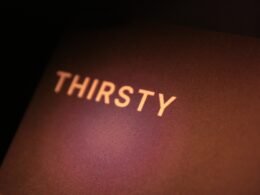 Das Wort "thirsty" steht weiß geschrieben auf einer dunkel gehaltenen Oberfläche, minimalistisch und klar fotografiert.