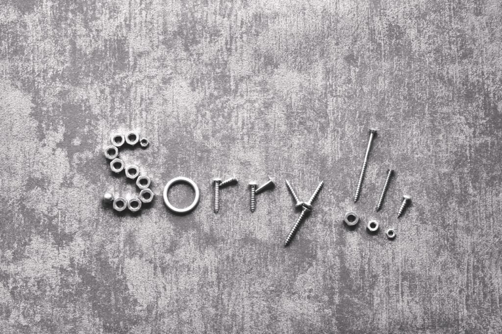 Das Wort sorry in metallenen Buchstaben auf einer grauen Betonwand, fotografiert von Michaela St
