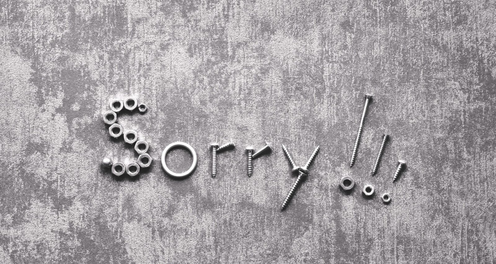 Das Wort sorry in metallenen Buchstaben auf einer grauen Betonwand, fotografiert von Michaela St