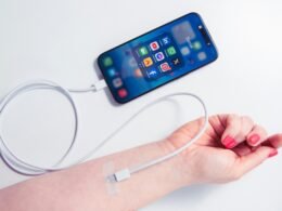 Nahaufnahme eines weiblichen Arms, der ein Smartphone hält, an das ein Ladegerät angeschlossen ist.